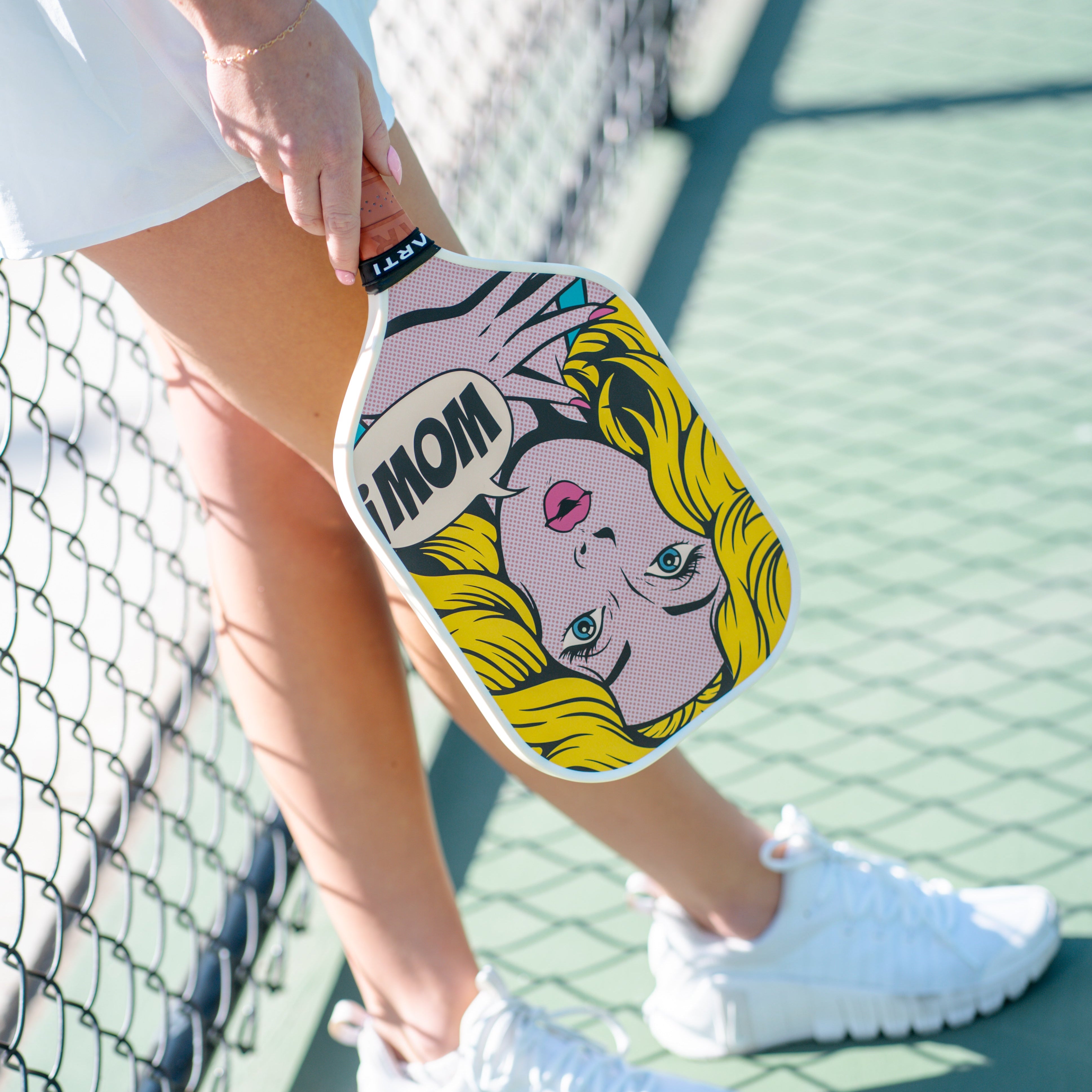 Player in white standing at a chain-link fence with the ARTI Wow pop-art paddle at her side