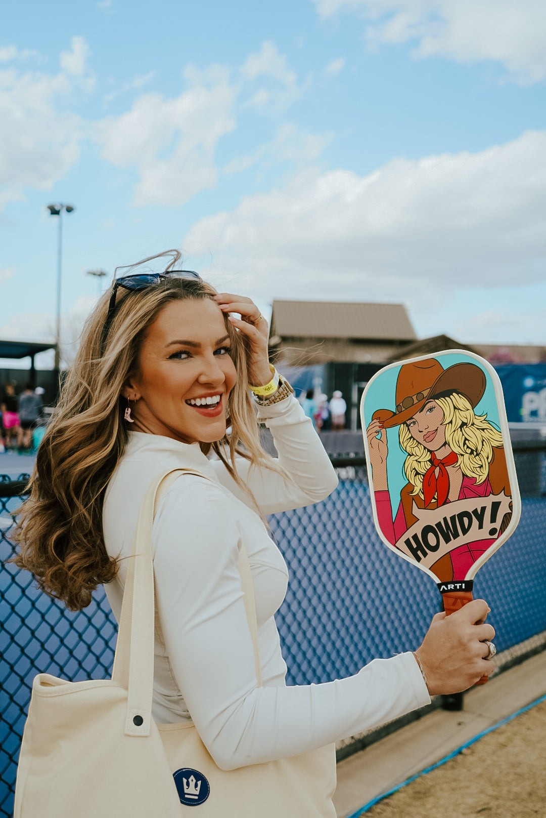 ARTI "HOWDY" pickleball paddle with pop-art cowgirl design, 16mm carbon fiber face, held by a smiling woman on a court.