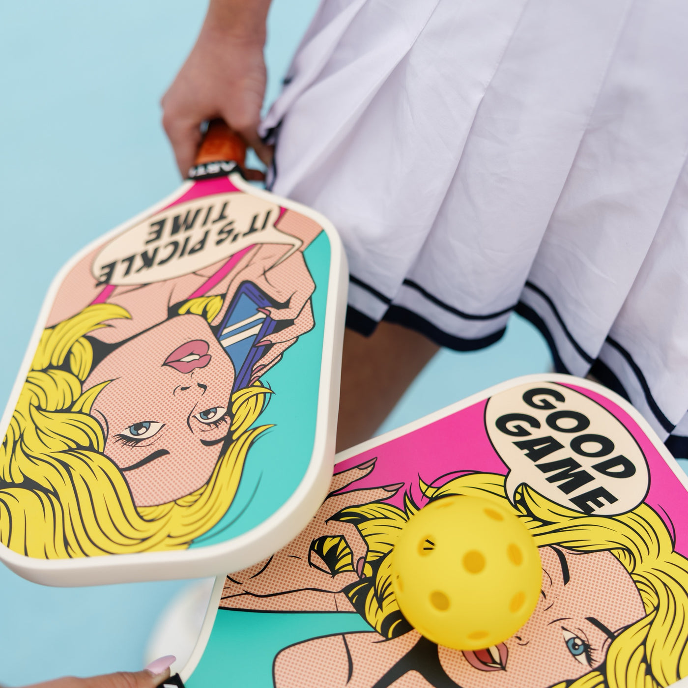 The Good Game and It's Pickle Time pop-art paddles with a yellow pickleball against a pale blue backdrop