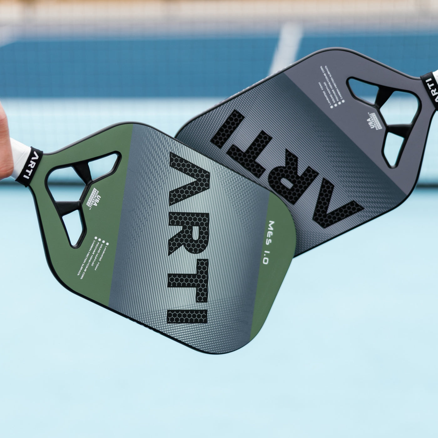 Two ARTI Mastery Elite MES 1.0 pickleball paddles tapped together over a court