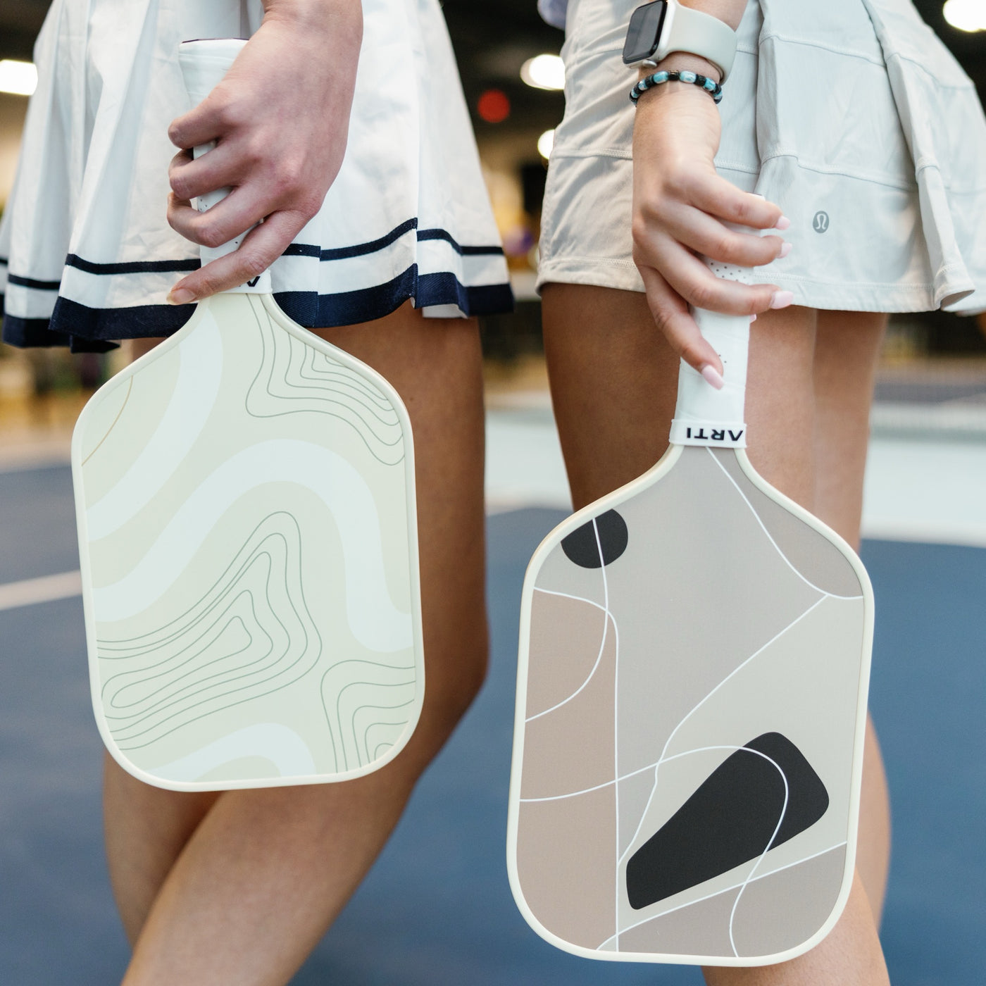 Two ARTI topo-print fiberglass pickleball paddles held courtside